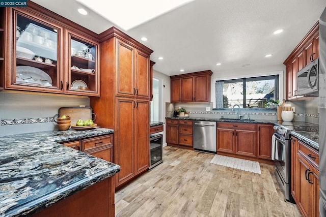 kitchen featuring sink, dark stone counters, stainless steel appliances, beverage cooler, and light hardwood / wood-style floors