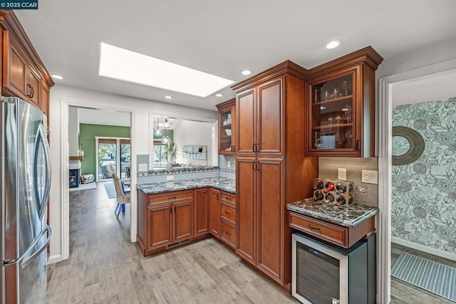 kitchen with stone countertops, light hardwood / wood-style flooring, stainless steel refrigerator, and a skylight