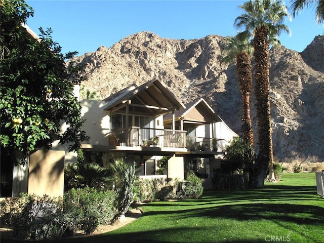 rear view of property featuring a mountain view, a lawn, and a balcony