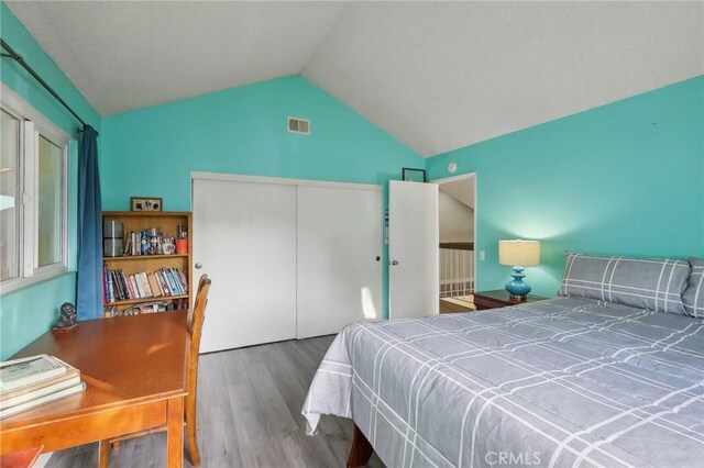 bedroom with wood-type flooring, vaulted ceiling, and a closet