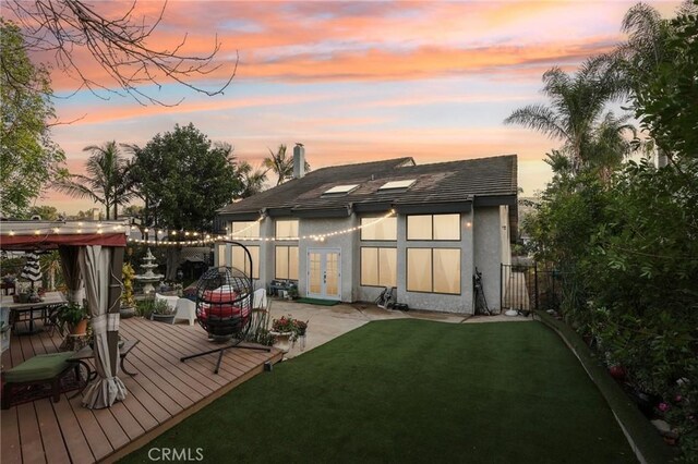 back house at dusk with a lawn and a deck