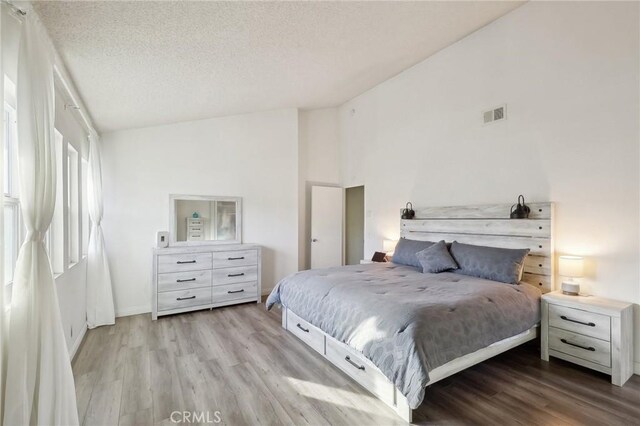 bedroom with vaulted ceiling, light hardwood / wood-style floors, and a textured ceiling