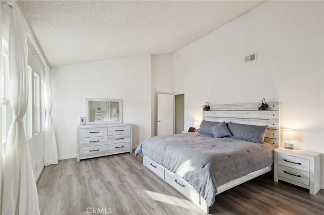 bedroom with visible vents, high vaulted ceiling, a textured ceiling, light wood-style floors, and baseboards