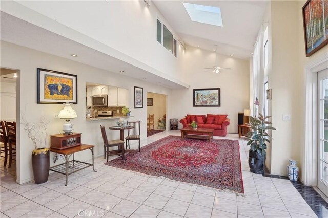 living room featuring a high ceiling, light tile patterned floors, ceiling fan, and a skylight