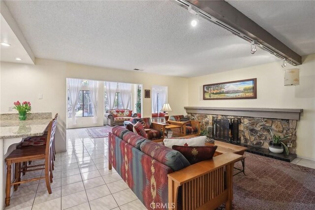 tiled living room featuring a stone fireplace, rail lighting, and a textured ceiling