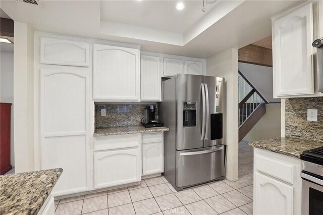 kitchen featuring tasteful backsplash, stone countertops, appliances with stainless steel finishes, a raised ceiling, and white cabinets