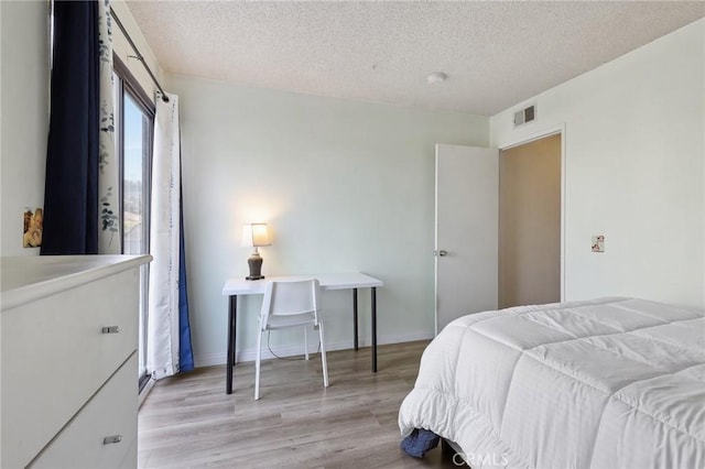 bedroom featuring visible vents, baseboards, a textured ceiling, and wood finished floors