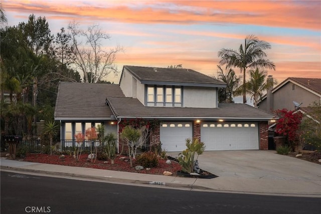 view of front facade with fence, driveway, stucco siding, a tile roof, and brick siding