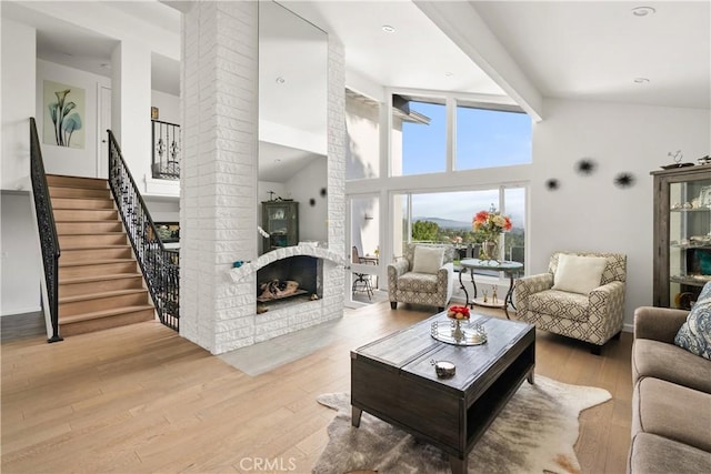 living area featuring decorative columns, wood finished floors, stairs, a brick fireplace, and high vaulted ceiling