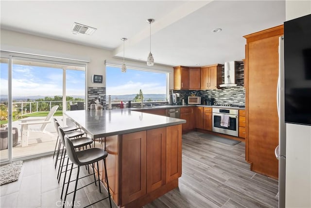 kitchen with visible vents, wall chimney exhaust hood, brown cabinets, a peninsula, and stainless steel appliances