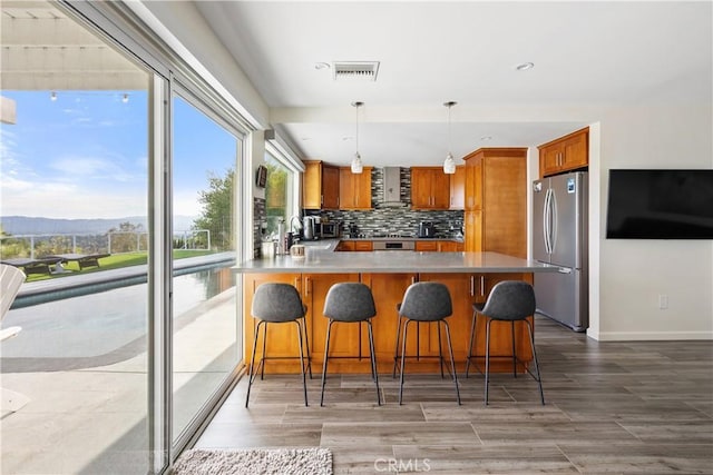 kitchen featuring tasteful backsplash, freestanding refrigerator, brown cabinetry, and visible vents