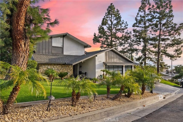 view of front of house featuring a shingled roof, stone siding, stucco siding, a front lawn, and board and batten siding