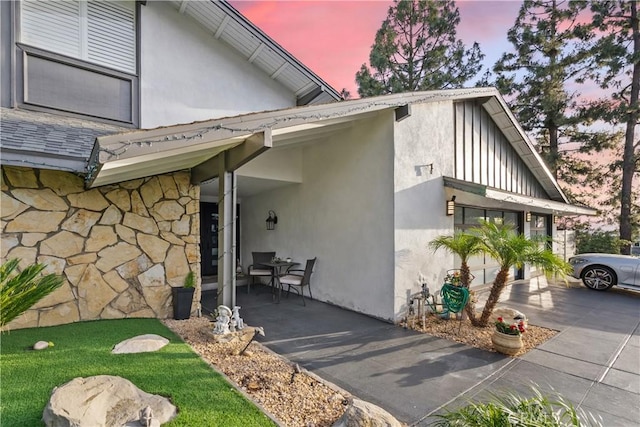 property exterior at dusk featuring stone siding, driveway, and stucco siding