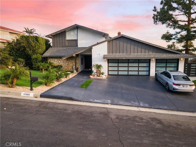 view of front facade featuring a garage, concrete driveway, a shingled roof, and stone siding