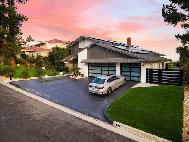 view of front facade featuring a garage, solar panels, aphalt driveway, and a front yard