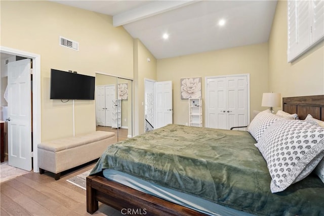 bedroom featuring high vaulted ceiling, wood finished floors, visible vents, beam ceiling, and two closets