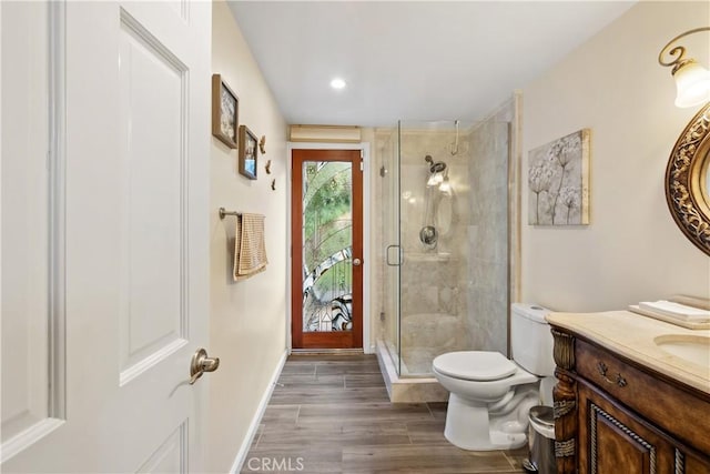 bathroom featuring toilet, wood finished floors, vanity, baseboards, and a stall shower