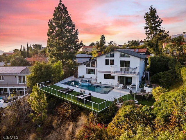 back of house at dusk with a patio, a fenced backyard, a balcony, and an outdoor pool