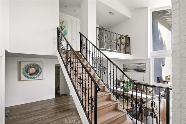 stairs with visible vents, a high ceiling, baseboards, and wood finished floors