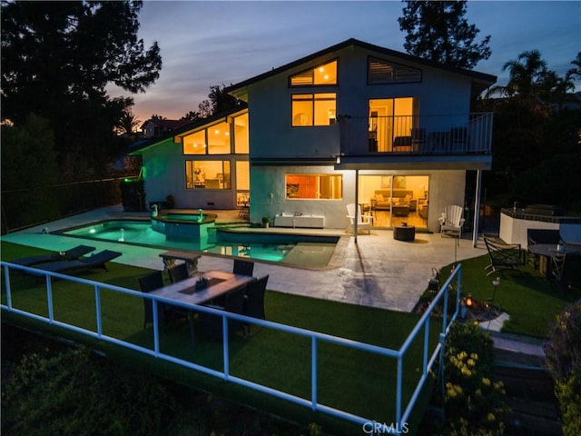 back of property featuring stucco siding, a pool with connected hot tub, a patio area, fence, and a balcony