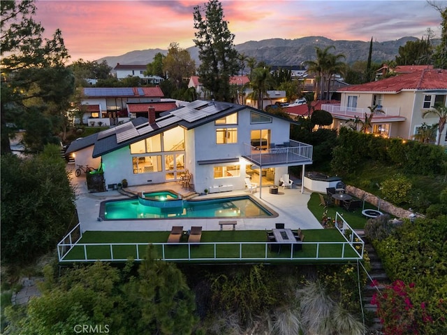 back of house at dusk featuring roof mounted solar panels, a fenced backyard, a mountain view, and a balcony