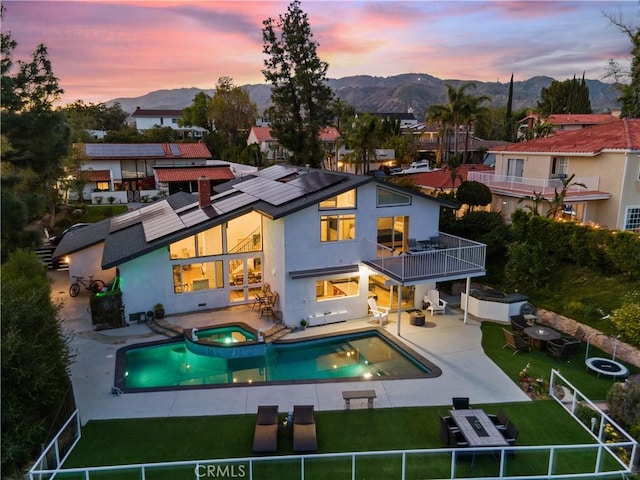 back of property featuring a balcony, a patio area, a mountain view, and solar panels