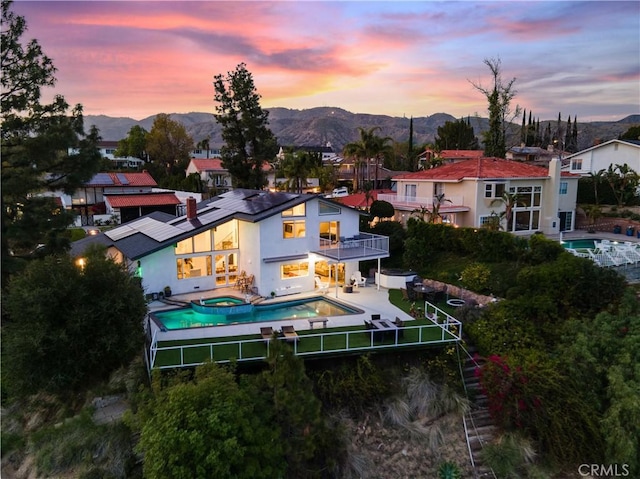 back of property featuring a mountain view, a pool with connected hot tub, a patio area, and a balcony