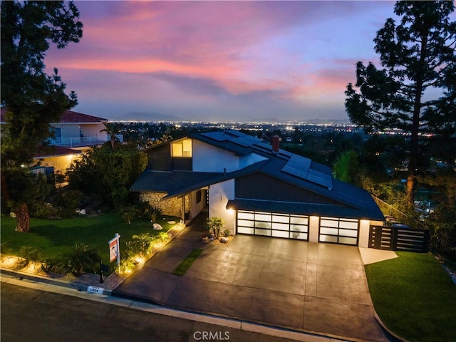 view of front of property with solar panels, concrete driveway, an attached garage, fence, and a front lawn