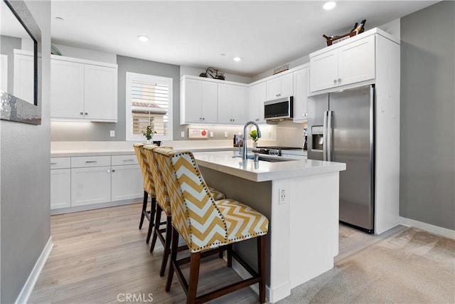 kitchen featuring appliances with stainless steel finishes, an island with sink, a breakfast bar, and white cabinets