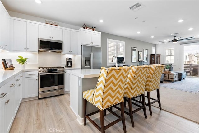 kitchen with appliances with stainless steel finishes, white cabinets, light hardwood / wood-style floors, a kitchen island, and a kitchen bar