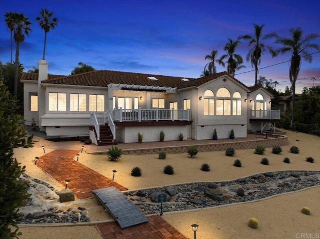 back house at dusk with a wooden deck and a patio area