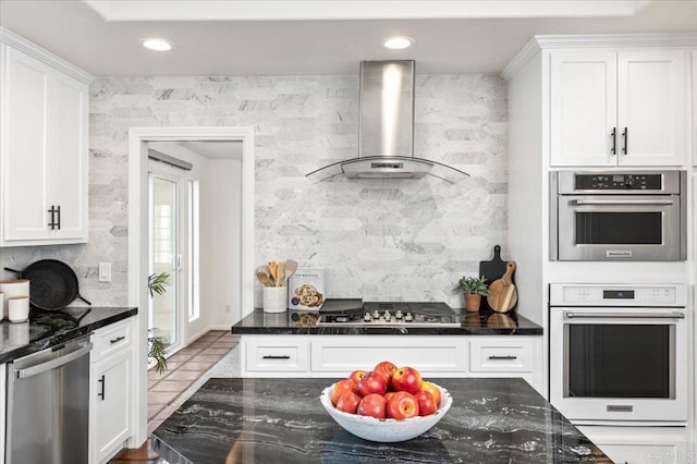 kitchen with dark stone countertops, wall chimney exhaust hood, stainless steel appliances, and white cabinets