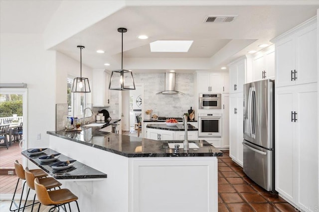 kitchen featuring wall chimney range hood, sink, appliances with stainless steel finishes, white cabinetry, and backsplash