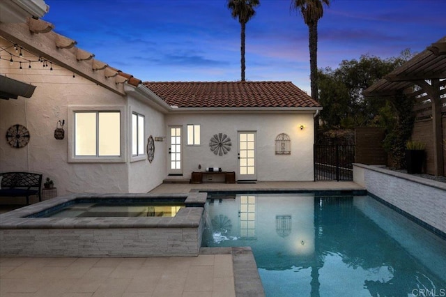 pool at dusk with an in ground hot tub and a patio area