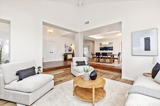 living room featuring an inviting chandelier, hardwood / wood-style flooring, beamed ceiling, and a towering ceiling