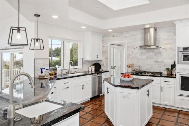 kitchen with wall chimney range hood, a kitchen island, sink, and appliances with stainless steel finishes