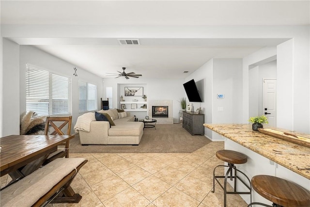 living area with a warm lit fireplace, visible vents, ceiling fan, and light tile patterned flooring