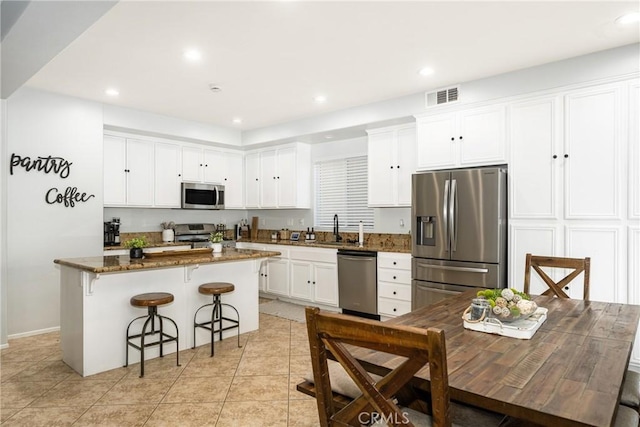 kitchen with dark stone countertops, appliances with stainless steel finishes, a center island, and white cabinets