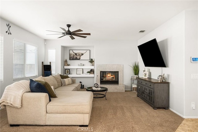 living room featuring visible vents, baseboards, a ceiling fan, light colored carpet, and a glass covered fireplace