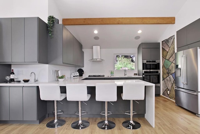 kitchen featuring stainless steel appliances, gray cabinetry, kitchen peninsula, and wall chimney exhaust hood