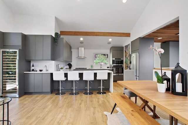 kitchen featuring a breakfast bar, gray cabinetry, beverage cooler, kitchen peninsula, and wall chimney exhaust hood