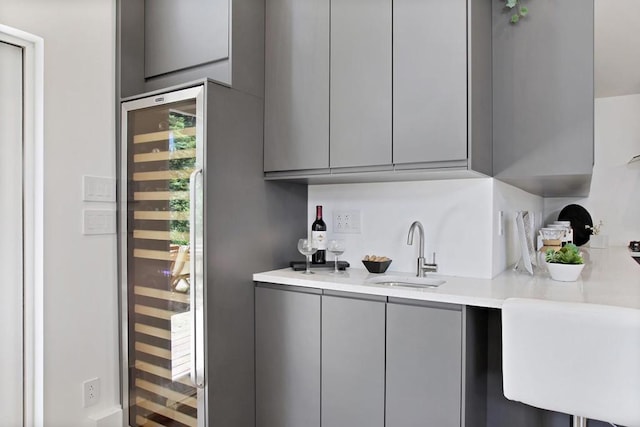 bar featuring gray cabinets, sink, and beverage cooler