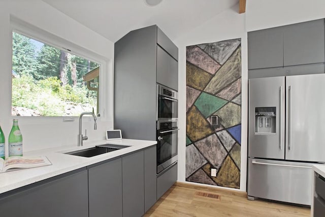 kitchen featuring gray cabinets, appliances with stainless steel finishes, sink, and light wood-type flooring