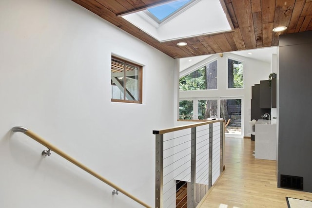 corridor with high vaulted ceiling, a skylight, light hardwood / wood-style floors, and wooden ceiling