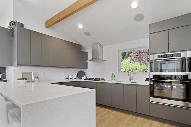 kitchen featuring sink, wall chimney range hood, kitchen peninsula, and gray cabinetry