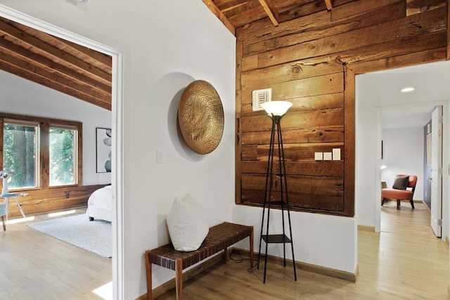 hall featuring lofted ceiling, light hardwood / wood-style flooring, wooden ceiling, and wood walls