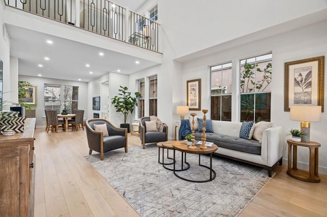 living room with a healthy amount of sunlight, light hardwood / wood-style floors, and a towering ceiling