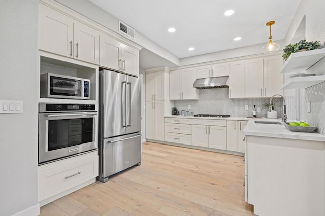 kitchen with sink, appliances with stainless steel finishes, white cabinetry, tasteful backsplash, and decorative light fixtures