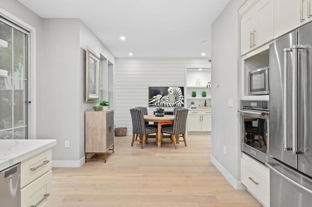 kitchen with light stone countertops, appliances with stainless steel finishes, white cabinets, and light hardwood / wood-style flooring