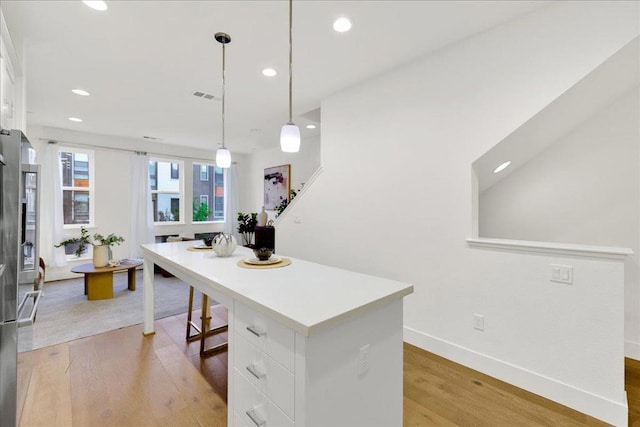 kitchen with white cabinetry, a kitchen island, light wood-type flooring, and decorative light fixtures